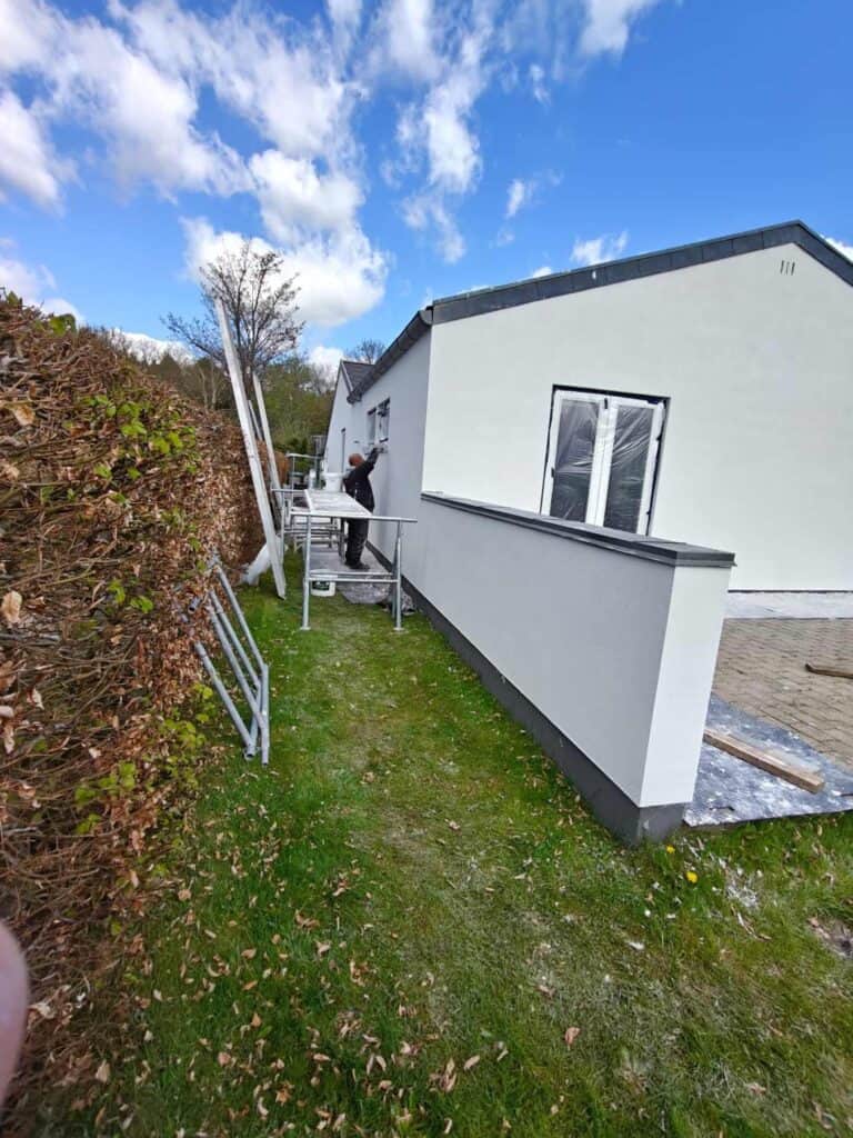 Håndværker på stige udfører netpuds facade på hvidt hus